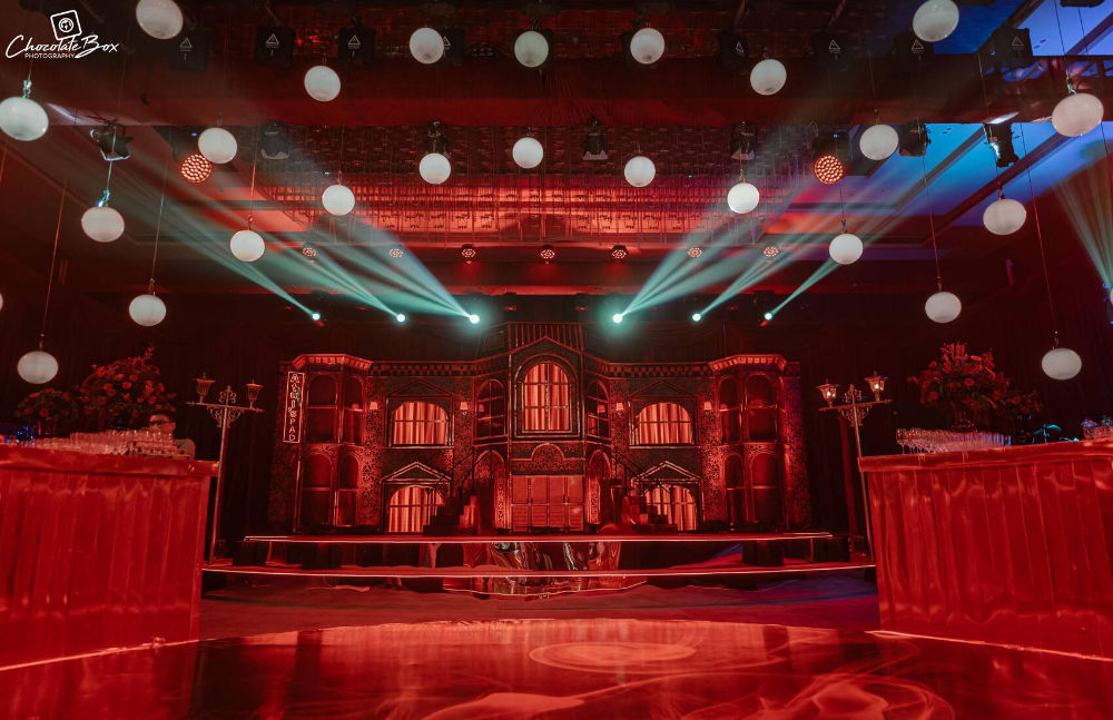 Elegant event venue with dramatic red lighting, ornate architectural backdrop, and ceiling lanterns creating a magical ambiance.