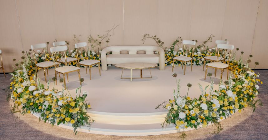 Elegant event stage with chairs, cream sofa, and vibrant yellow and white floral arrangements.