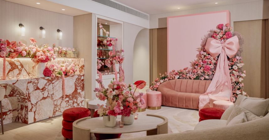 Elegant room with floral decor, pink couch, and marble counter, featuring large pink bow and soft lighting.