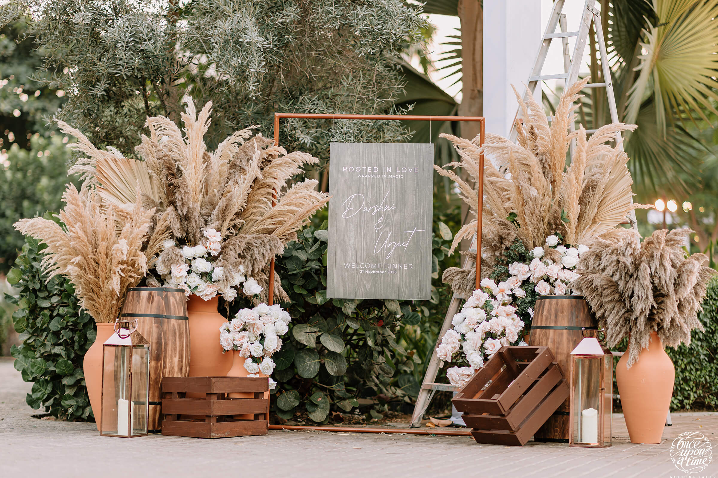 Boho wedding decor with pampas grass, white roses, wooden crates, and lanterns, creating a rustic chic ambiance.